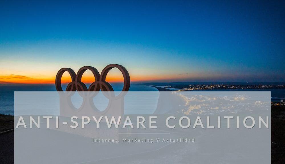 Scenic sunset view of the Olympic rings monument by the sea with city lights in the distance.
