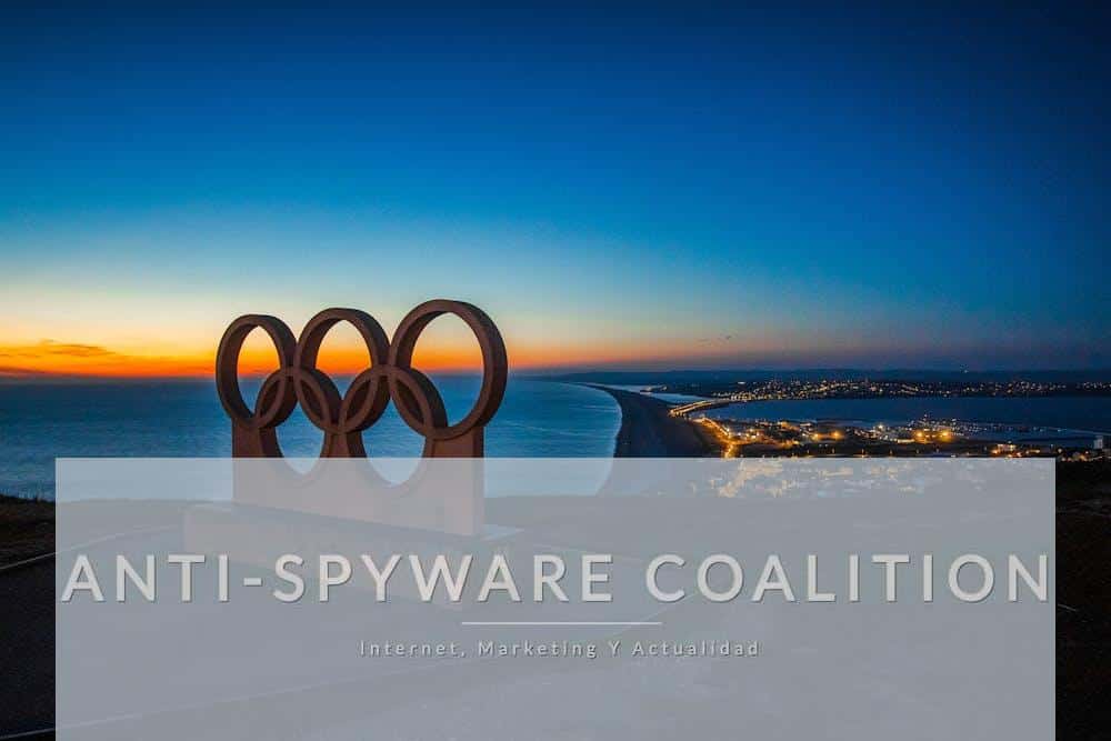 Scenic sunset view of the Olympic rings monument by the sea with city lights in the distance.