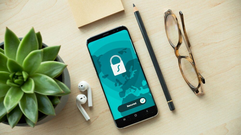 Móvil con un candado en pantalla junto a unas gafas, símbolo de cómo eliminar el spyware del móvil