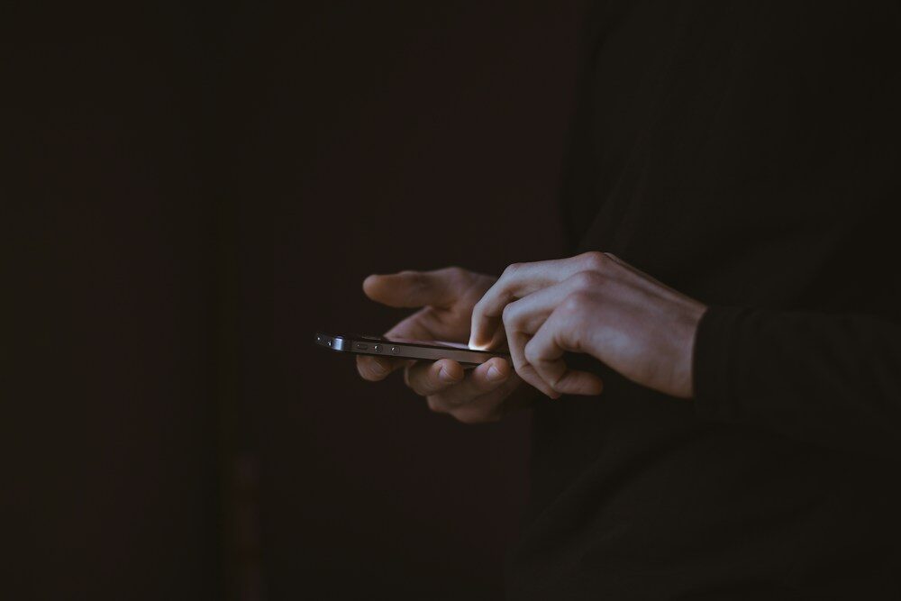 Manos sujetando un móvil en la oscuridad, la situación típica del spyware que espía el teléfono